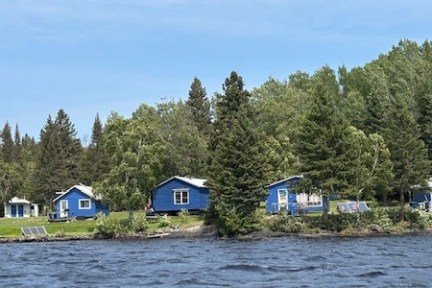 Blue cabins by a forested lakeshore on a clear day.