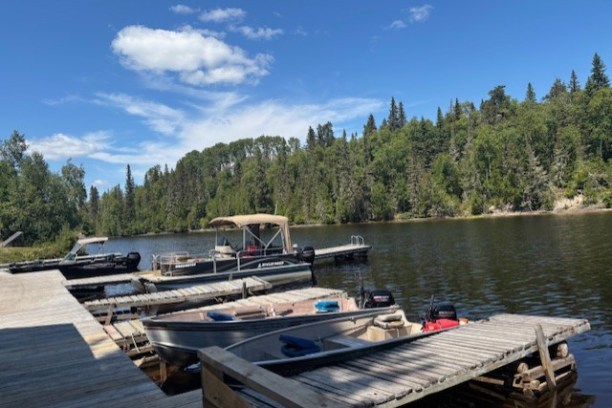 Boats docked at a wooden pier on a calm lake with a forested shoreline.