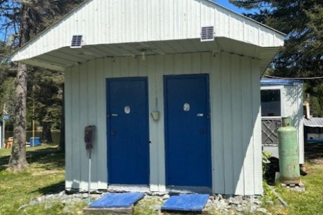 Small building with two blue doors in a grassy area, surrounded by trees.